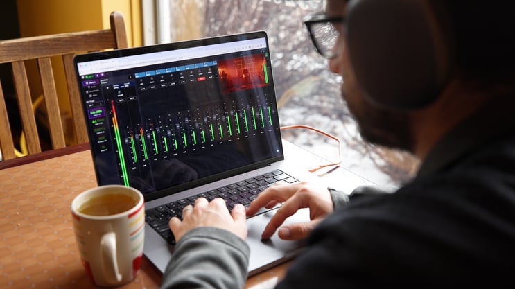 Man mixing audio on a laptop sitting at a coffee shop