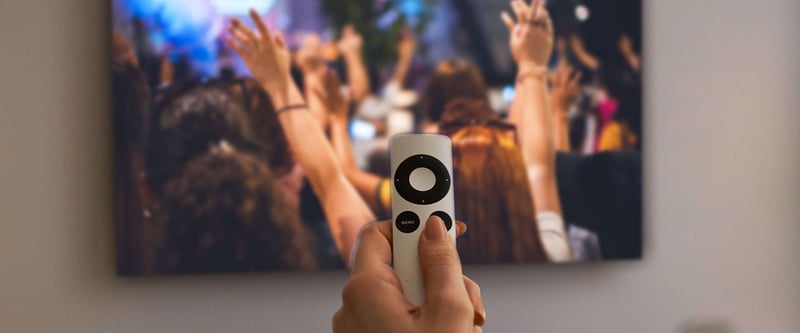 Person holding remote and watching live stream of a concert on an Apple TV