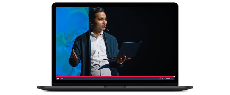 Person speaking on stage at a virtual conference, streamed live on a laptop