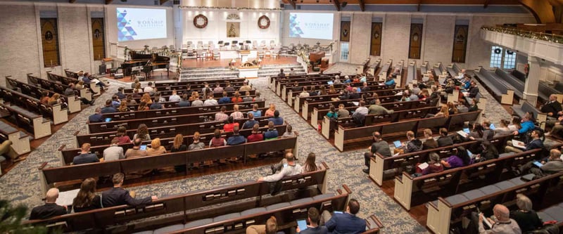 Church pews full of people facing the stage full of instruments