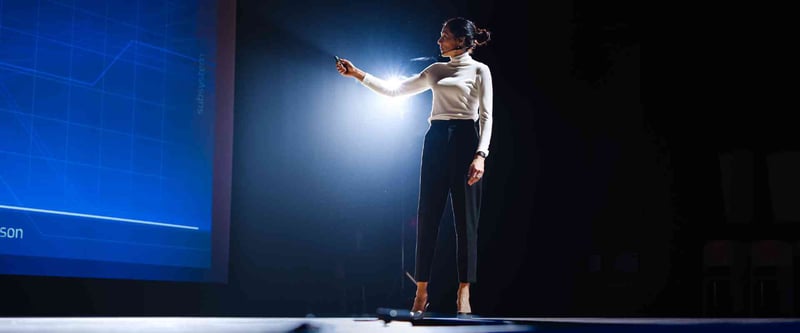 Medium shot of a presenter on a stage with partial view of the backdrop