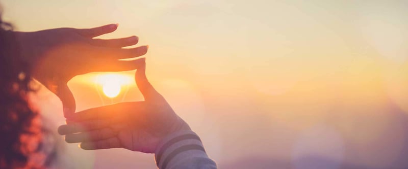 hands making a silhouetted frame shape in front of a sunset