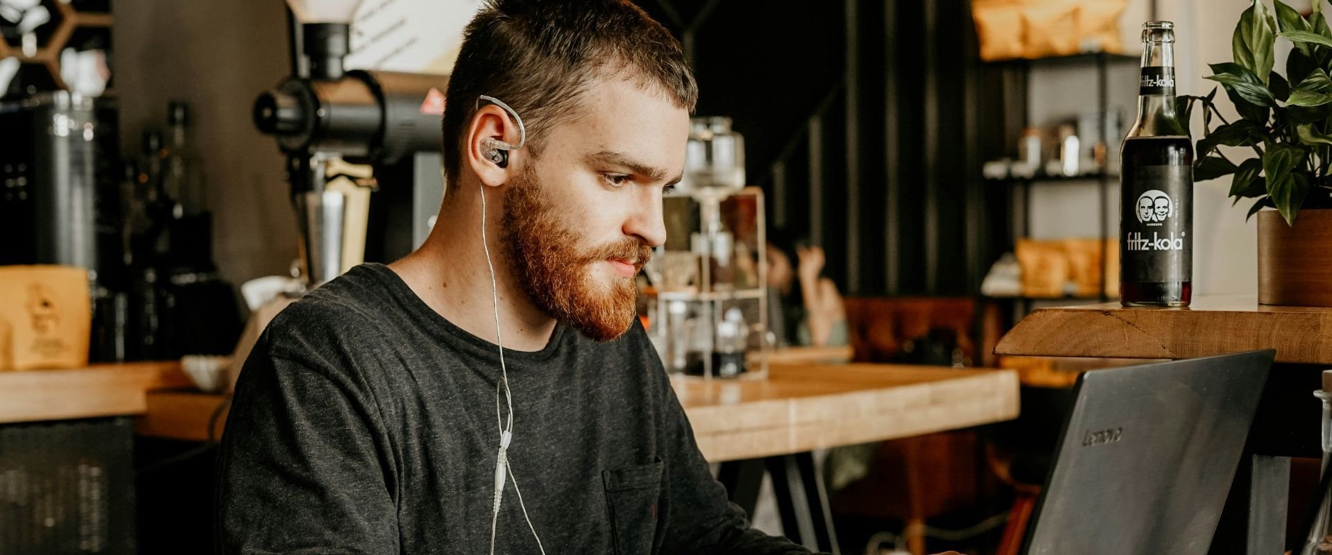 A man wearing in-ear headphones working behind a laptop screen