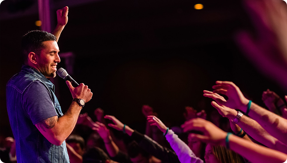 Pastor speaking to a crowd with arms raised during a church worship service