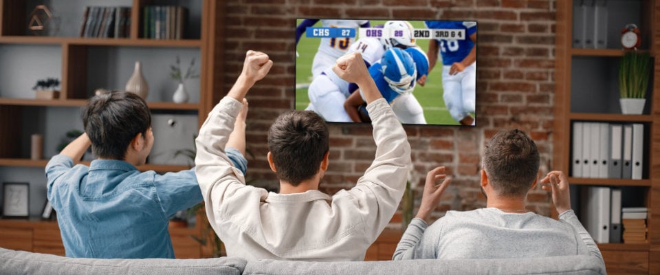 3 people sitting on a couch watching a football game