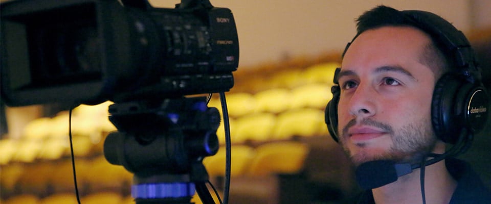 Videographer with headset on filming a live event with a camera in an auditorium