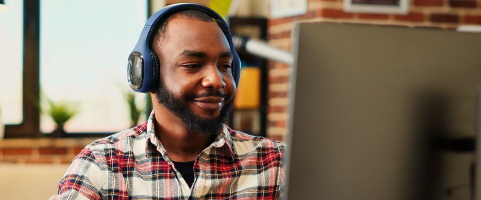 A man wearing headphones and looking at a laptop screen