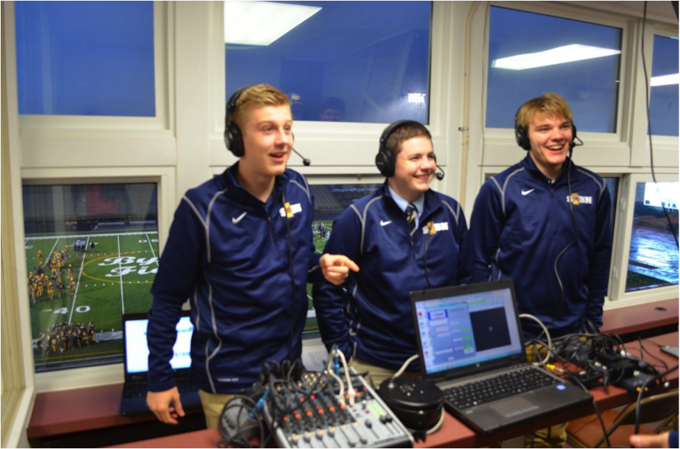 Three students with headsets stand in front of camera